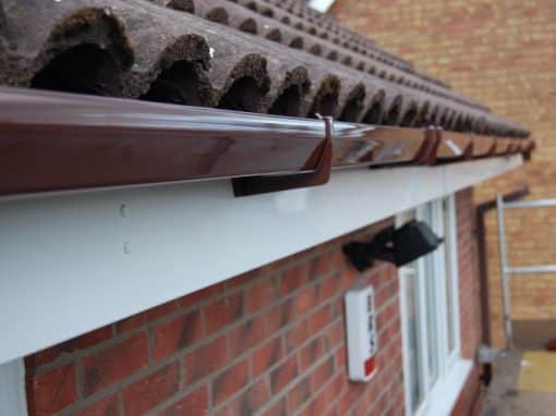 Oswestry Roofing Services New brown guttering secured beneath roof tiles with a clean white fascia board for roofing work in Oswestry