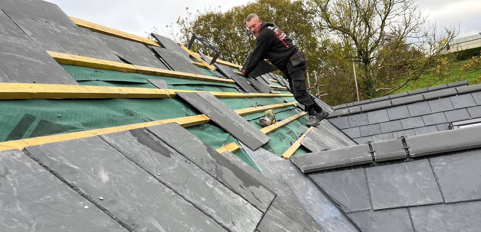 Oswestry Roofing Services Roof Repairs Header Professional roofer carrying out roof repairs, new roofs and roofline work on a residential slate roof in Oswestry, working over new membrane and timber battens